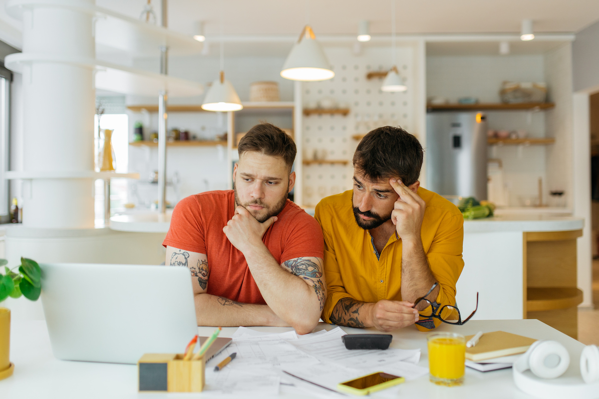 Gay male couple looking at bills on computer.