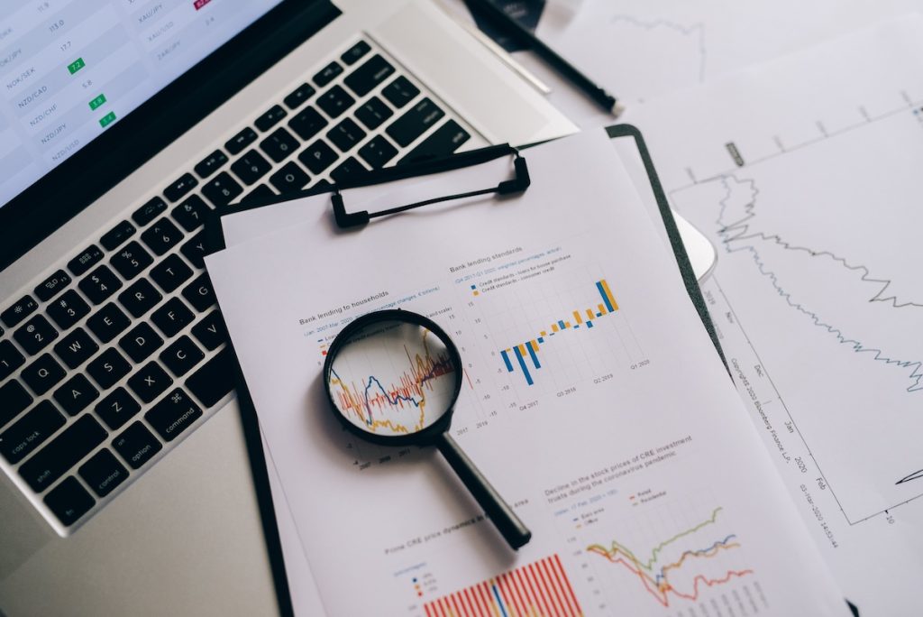Magnifying glass, computer keyboard, and papers with stock market trends on them.