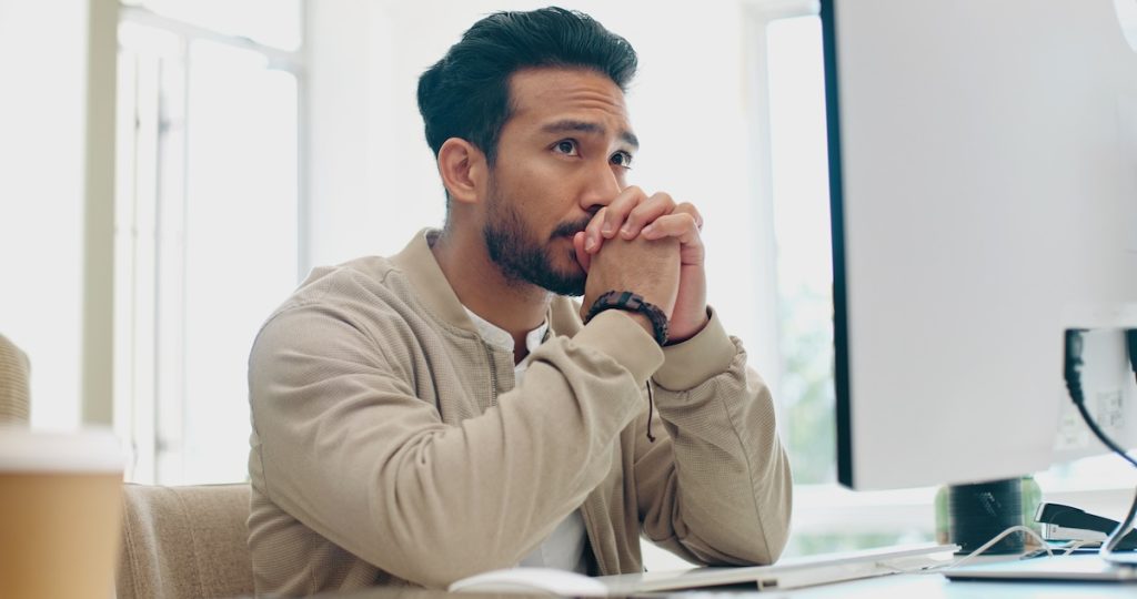 Man sitting at desk in front of computer looking stressed